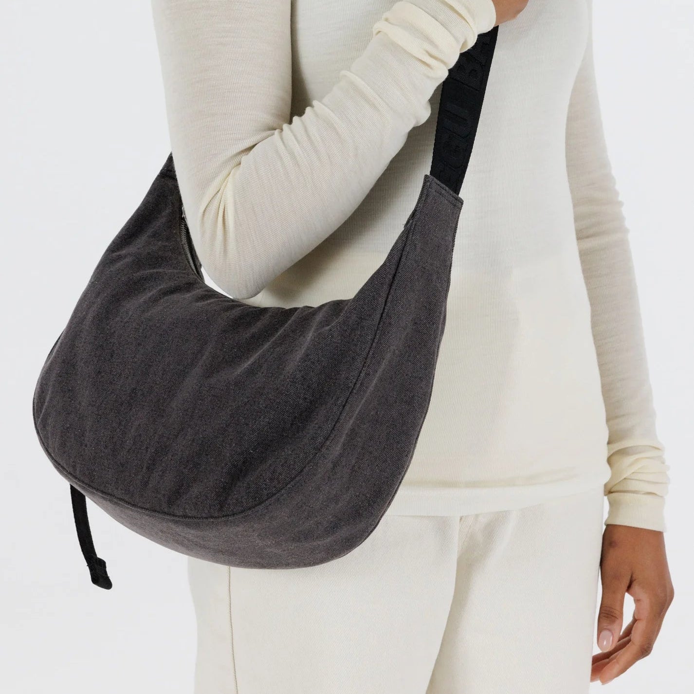 Person holding a black denim shoulder bag against a white background