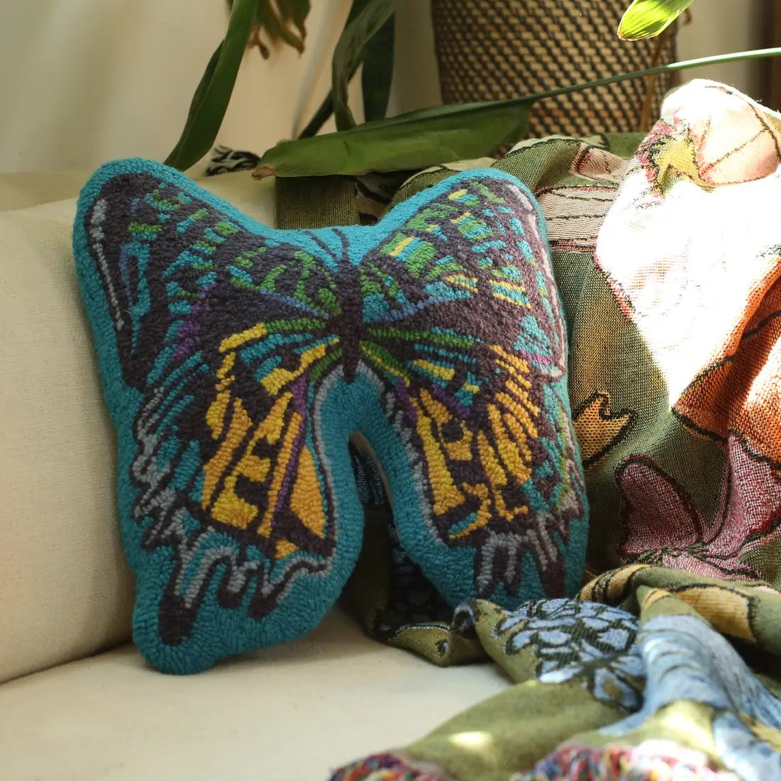 A blue butterfly-shaped decorative throw pillow with a zipper at the back, placed on a sofa next to a colorful scarf.