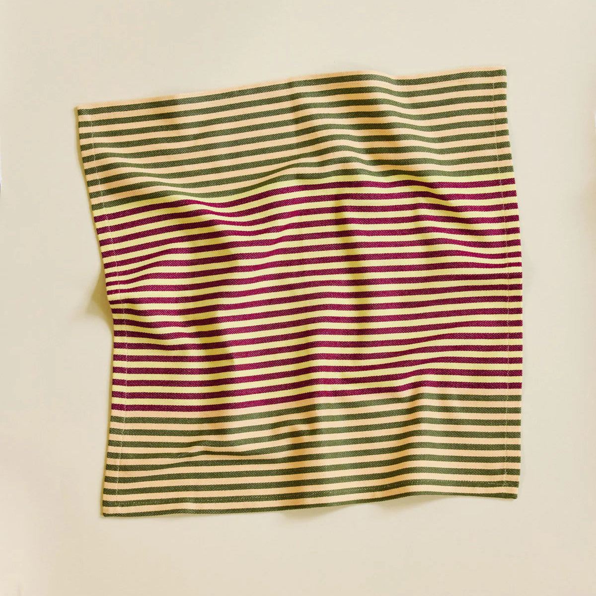 Striped fabric napkin with green and purple stripes on a beige background