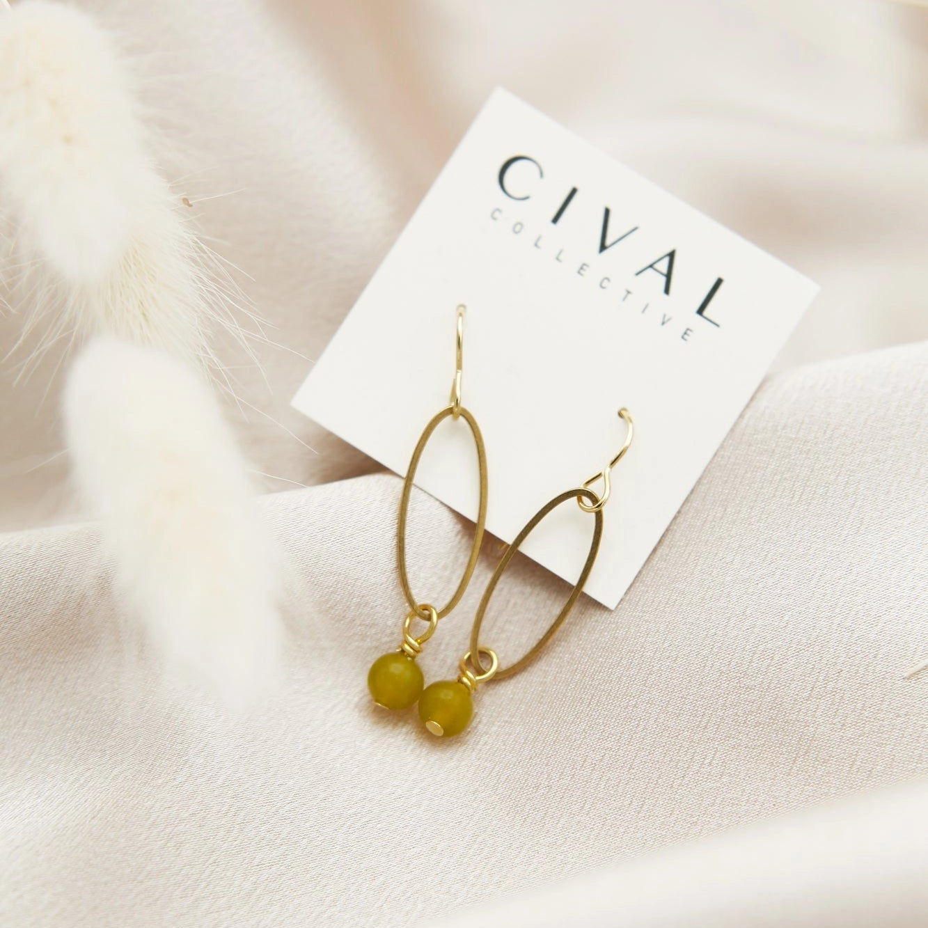 Gold earrings with green beads on a Cival Jewelry card against a soft beige background