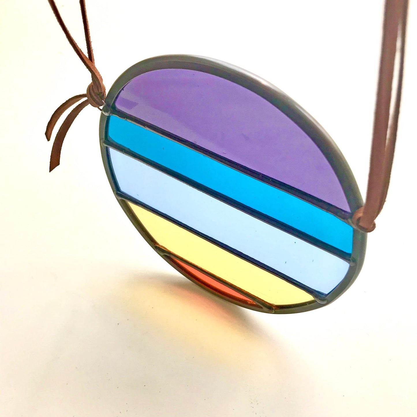 Colorful striped pendant on a brown cord against a white background