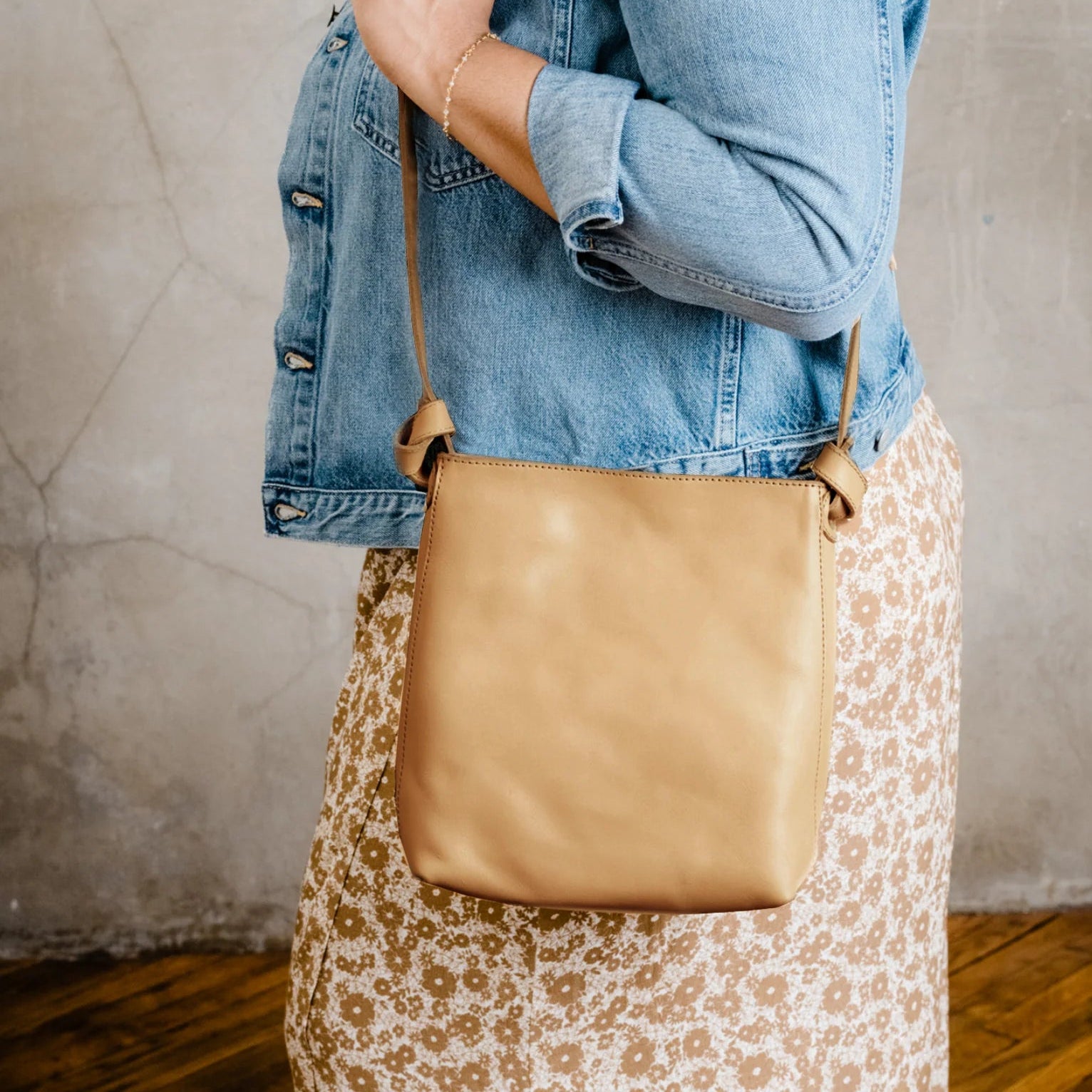 Person holding tan leather shoulder bag.