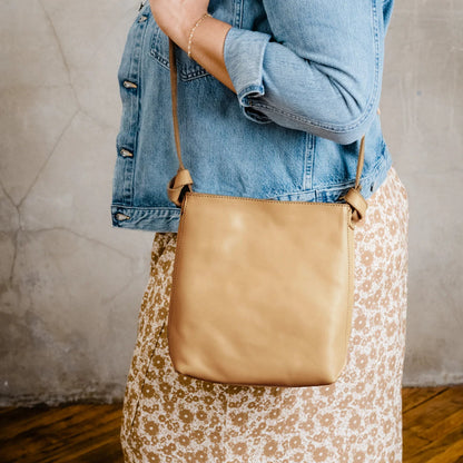 Person holding tan leather shoulder bag.