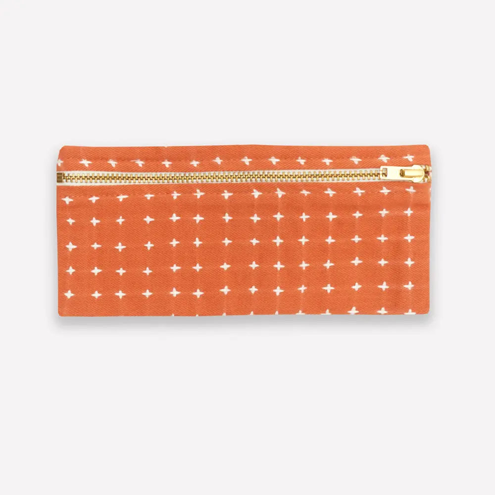 Orange pencil case with white cross stitch pattern and gold zipper on a white background