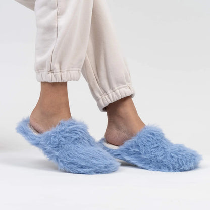 Blue fuzzy slippers worn with light-colored pants on a white background