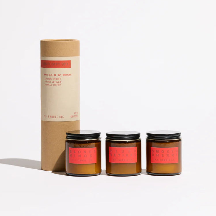 Three small soy wax candles with red labels and a cardboard tube on a white background