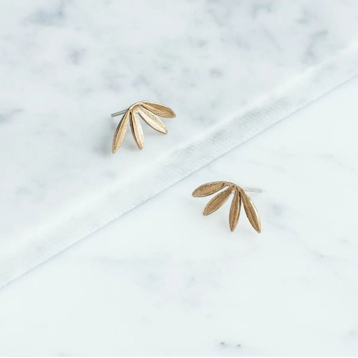 Gold leaf-shaped earrings on a marble surface