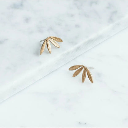Gold leaf-shaped earrings on a marble surface