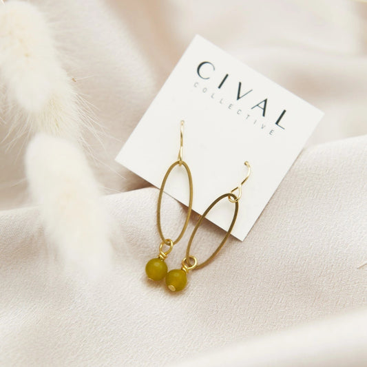 Gold earrings with green beads on a Cival Jewelry card against a soft beige background