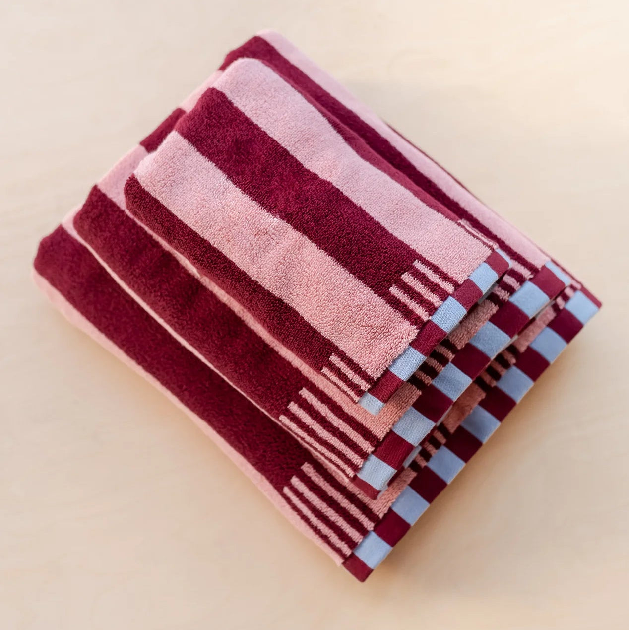 Stack of striped red & pink towels on a beige background