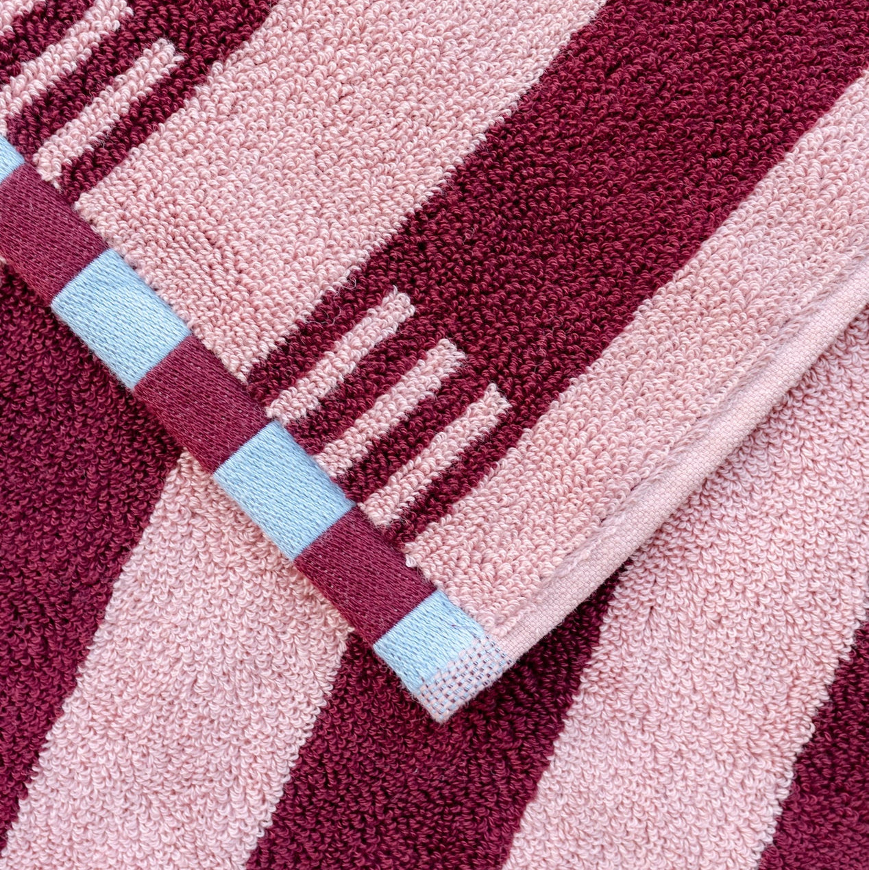 Close-up of a textured fabric with pink and red stripes and a blue square.