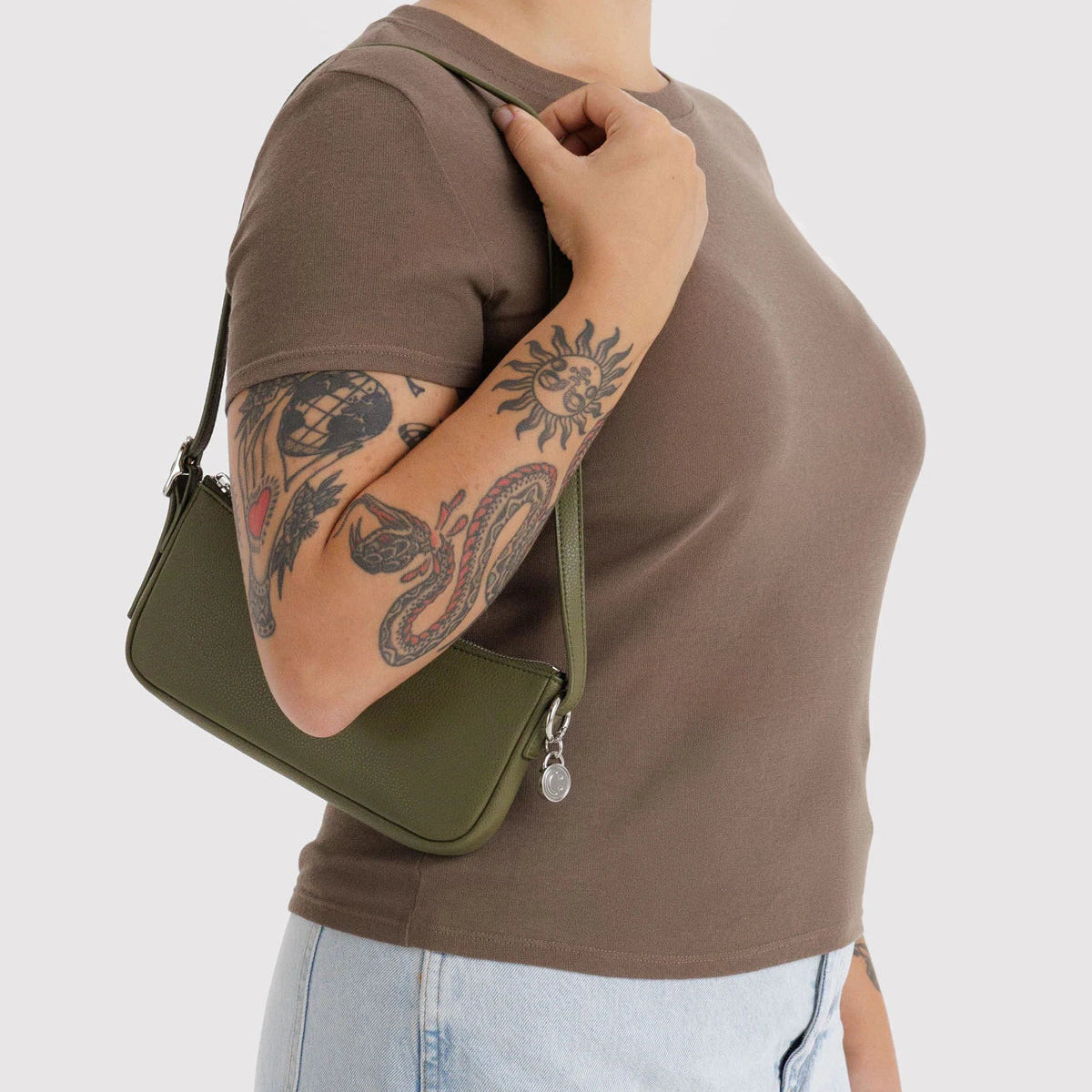 Person wearing a brown shirt and holding a green leather bag on a light gray background