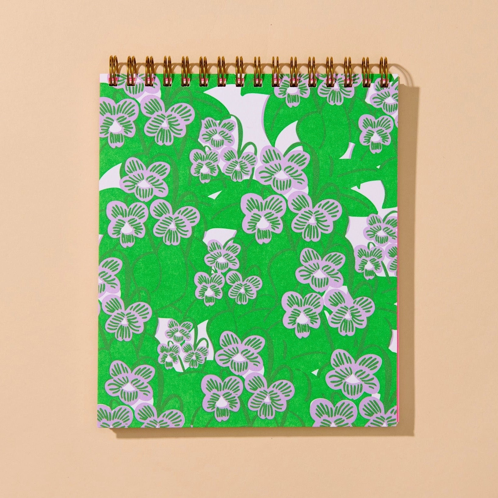 A spiral-bound notebook with a bright green cover featuring a white floral pattern, shown against a solid beige background.