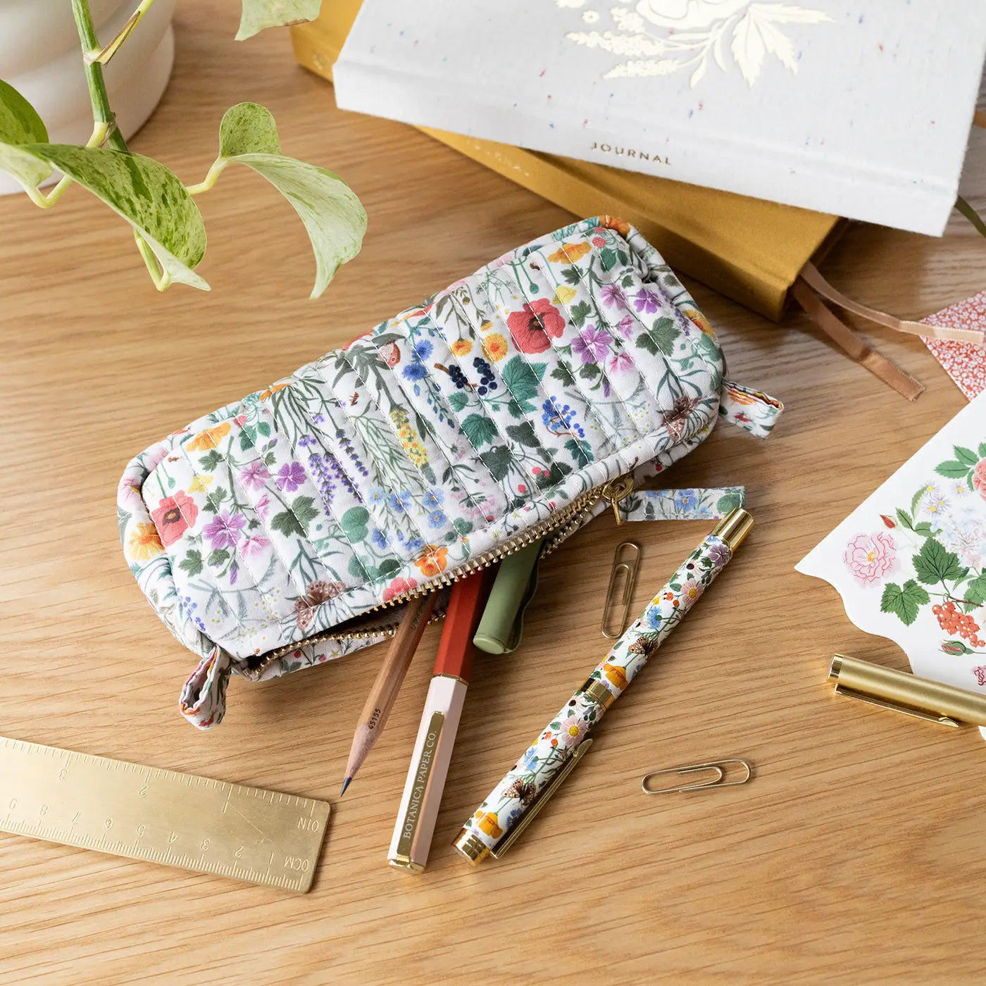 Floral pencil case with pens and paper clips on a wooden surface