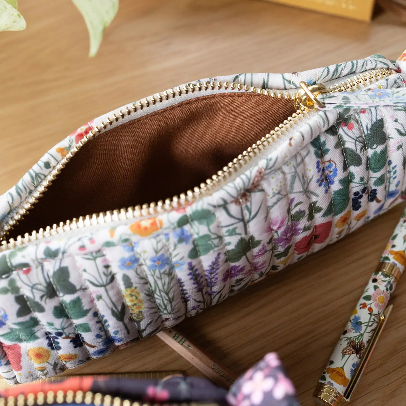 Floral-patterned pencil case with a gold zipper on a wooden surface